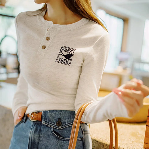 Person wearing a beige long-sleeve shirt with a logo, sitting outdoors.